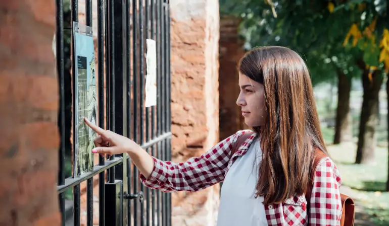 Woman interacting with a touchscreen gate access control system mounted on an iron gate outdoors.
